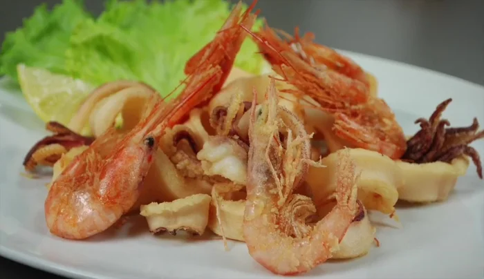 Servite la frittura di pesce calda con spicchi di limone, insalata e pane.
