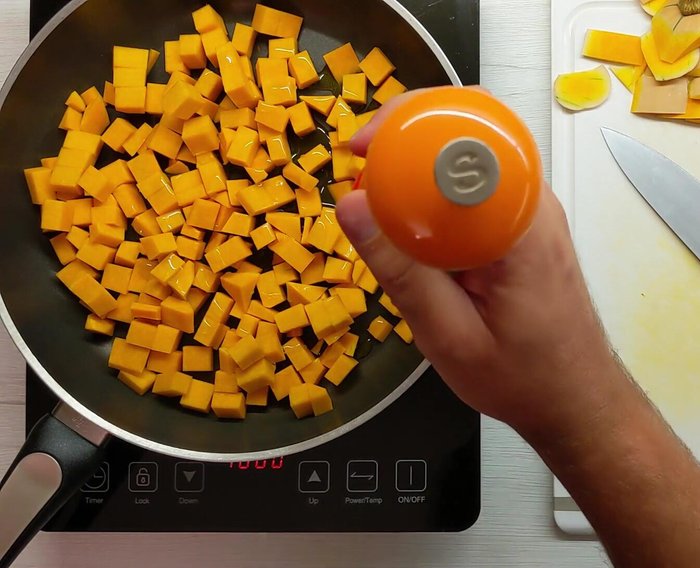 Trasferire i cubetti di zucca in una padella con un filo d'olio e una macinata di sale. Cuocere a fuoco moderato con il coperchio per 10-15 minuti, mescolando di tanto in tanto per evitare che si bruci.