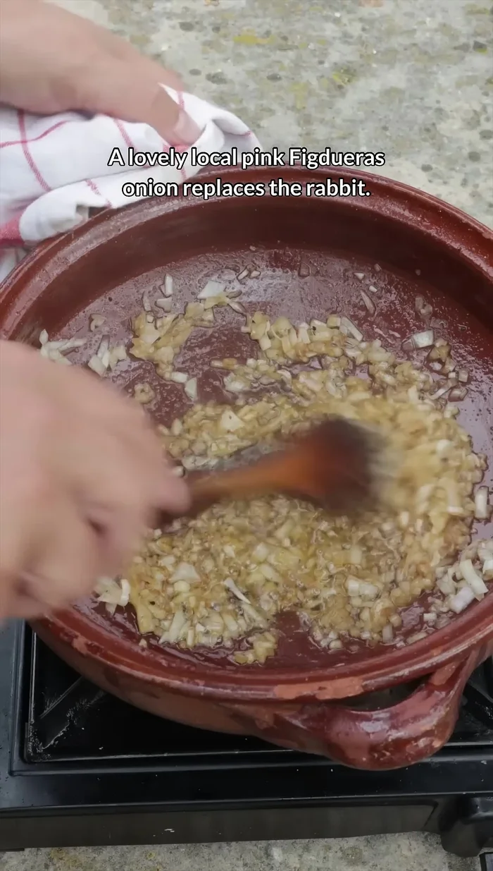 Aggiungere una cipolla rosa di Figueras, lasciar ammorbidire, poi rimettere il coniglio, mescolare per un minuto.