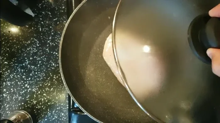 Aggiungere gli spicchi d'aglio schiacciati sopra il pollo e continuare la cottura per altri 2 minuti con il coperchio.