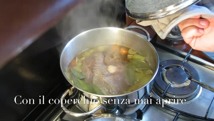 Cottura dell'arrosto: spostare la pentola su fuoco basso, aggiungere il brodo fino a metà altezza della carne. Cuocere per 2 ore a fiamma bassissima con il coperchio, senza mai aprirlo.