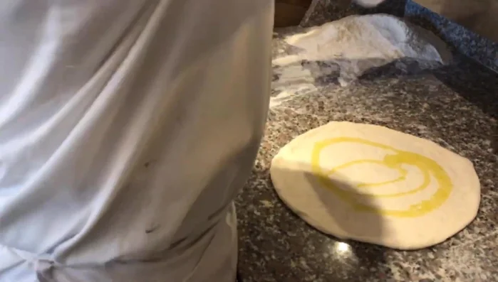 Preparare la pan focaccia: aggiungere olio, aglio e rosmarino all'impasto e stenderlo.