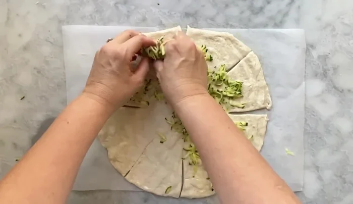 Farcire la pizza: Distribuire le zucchine ben strizzate su tutta la superficie (186.56). Aggiungere la mozzarella e lo speck solo all'interno degli spicchi (198.09, 201.72, 220.93). Aggiungere pepe.