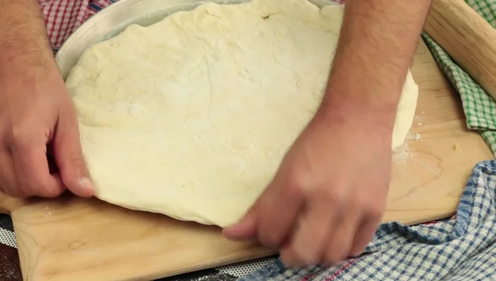 Stendere l'impasto della pizza leggermente più largo della teglia, per creare un bordo alto. [56.44]