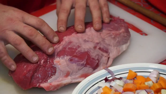 Lardellare la noce di vitellone: Incidere la carne lungo la fibra, inserire piccoli pezzi di lardo e legare con il filo da cucina.