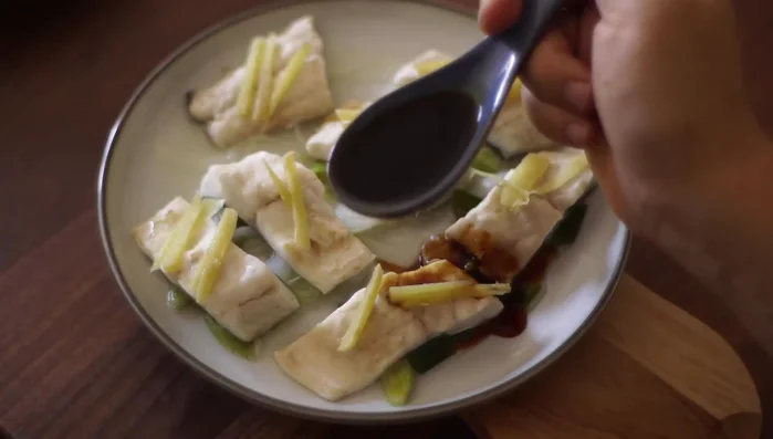 Versare un cucchiaio di salsa di soia sui filetti di branzino. (68.25)