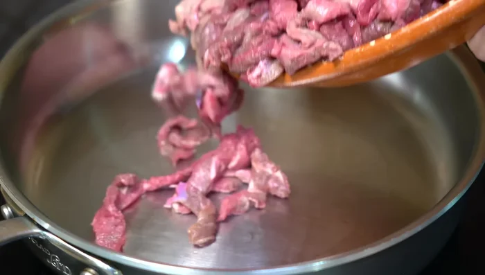 In una padella con olio caldo, rosolare la carne a fuoco alto per 7-8 minuti, poi abbassare la fiamma e aggiungere l'aglio tritato.