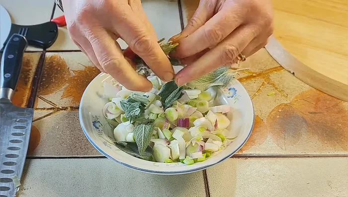 Taglia le cipolle o i cipollotti e mettili in una ciotolina. Aggiungi la salvia spezzettata, il pepe nero macinato, un filo d'olio extravergine di oliva e un pizzico di sale. Mescola bene e lascia insaporire.