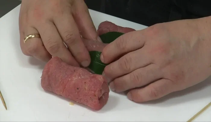 Posizionare una foglia di alloro tra gli involtini per aroma e colore (135.56). Chiudere con la foglia e fermare con gli spiedini (143.879). Condire con sale, pepe e olio extravergine di oliva (154.16). Lasciare insaporire (164.879).