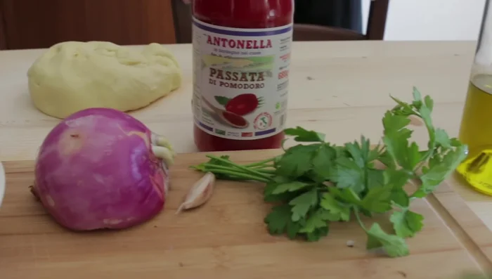 Preparare il ragù di pollo: soffriggere cipolla, aglio e prezzemolo, aggiungere vino bianco e passata di pomodoro.