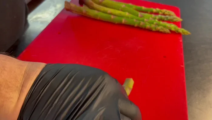 Lavare accuratamente gli asparagi. Prendere gli asparagi per le punte e piegarli a metà. Si romperanno nel punto in cui finisce la parte tenera e inizia quella dura. Eliminare la parte inferiore dura. Tagliare la parte superiore a rondelle e le punte in quattro per il lungo.