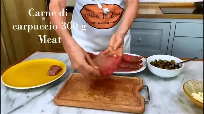 Su un tagliere, disponete le fette di carne di carpaccio.