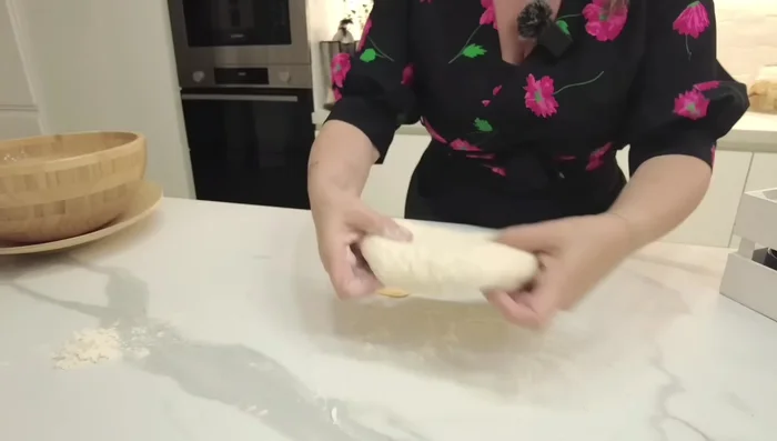 Infarinate la superficie di lavoro e stendete l'impasto lievitato, facendo le pieghe di rinforzo per dare forza all'impasto.