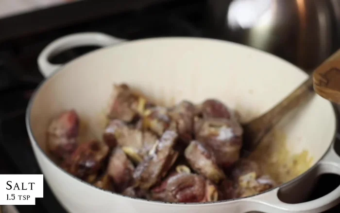 Rimettere l'agnello nella pentola. Condire con sale, pepe, pomodori pelati (o freschi grattugiati) e acqua, fino a coprire la carne.