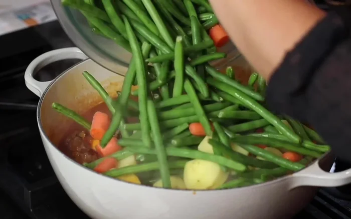 Dopo 45 minuti, aggiungere i fagiolini, le patate e le carote allo stufato. Condire con sale, aneto secco e mescolare.