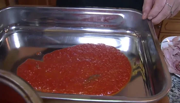 Componiamo la pasta nella teglia: uno strato di salsa, poi la pasta, le melanzane, la mozzarella, il basilico, il parmigiano e il prosciutto cotto. Ripetiamo gli strati.