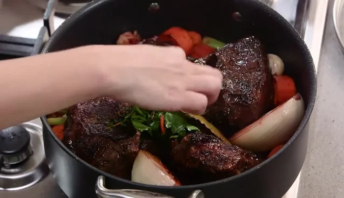 Nella pentola dal fondo spesso, unire le guance di manzo rosolate, le verdure, il bouquet garni, la scorza d'arancia, il concentrato di pomodoro, il vino rosso e il brodo di manzo.