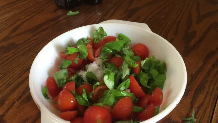 Unire i pomodori, il basilico, l'aglio, il sale, il pepe, l'aceto balsamico e l'olio extravergine di oliva in una ciotola. Mescolare bene, usando lo schiacciapatate per emulsionare l'olio e l'aceto e far uscire il succo dai pomodori.