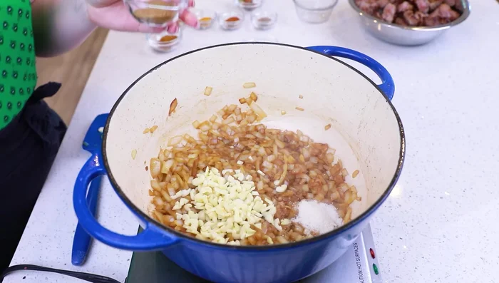 Aggiungere aglio affettato e tutte le spezie (sale, coriandolo, polvere di curry, cardamomo, peperoncino, curcuma, cumino, cannella, stecche di cannella, foglie di alloro, stella di anice). Cuocere per un paio di minuti.