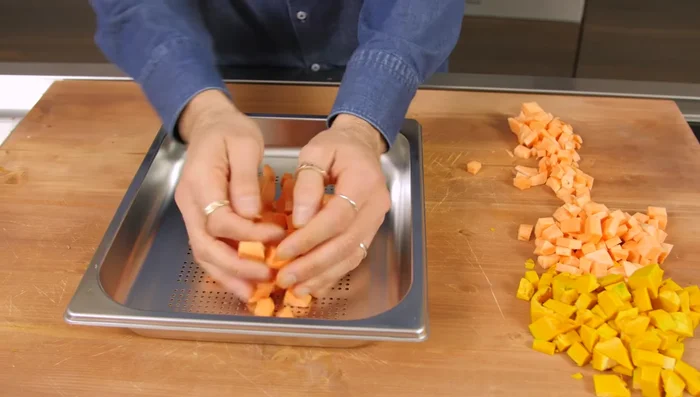 Distribuire patate e zucca su una teglia forata.