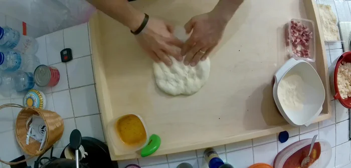 Stendere l'impasto per pizza sul piano di lavoro, creando un disco sottile con il cornicione.