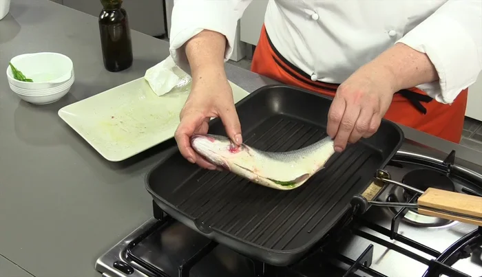 Posizionare la spigola sulla piastra (parte a vista verso l'alto). Cuocere per 1 minuto e mezzo per lato, poi inumidire con la miscela di acqua, olio e sale usando un ciuffetto di prezzemolo.