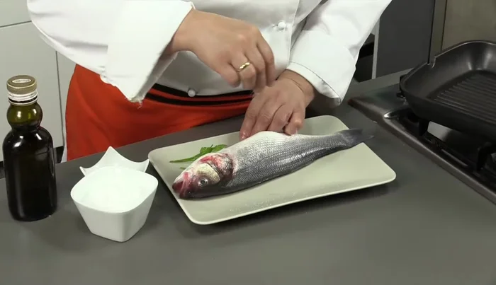 Condire la spigola: salare, pepare, inserire nel ventre uno spicchio d'aglio e un rametto di prezzemolo. Ungere con olio extravergine d'oliva delicato.