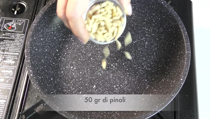 Tostare i pinoli in una padella antiaderente a fuoco basso per pochi minuti, mescolando continuamente.