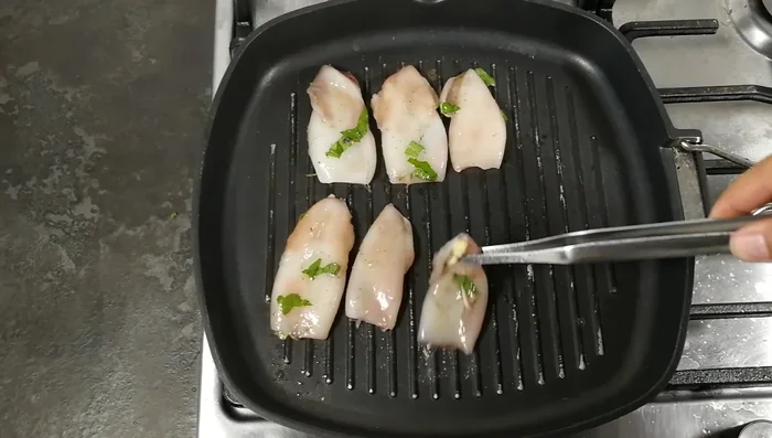 Posizionate i corpi dei calamari sulla griglia calda e cuocete per circa 3 minuti per lato, fino a quando si forma una crosticina dorata.