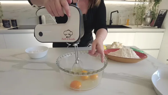 In una ciotola, montare le uova intere con lo zucchero a velo e un pizzico di sale. Aggiungere la scorza grattugiata di un limone non trattato.