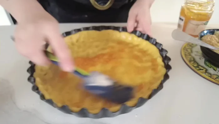 Distribuite la confettura di albicocche (o pesca) sulla base della crostata.