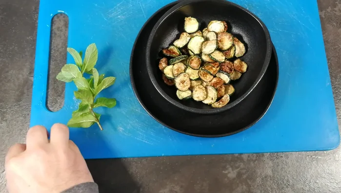 In un contenitore, mettere le zucchine fritte, l'aglio, le foglioline di menta fresca spezzettate, un filo d'olio extravergine di oliva, sale e pepe.