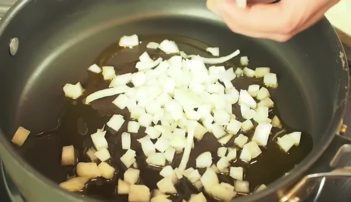 In una padella bassa, preparare la salsa: aggiungere olio, cipolla tagliata a cubetti e rosolare per circa 5 minuti a fuoco medio.