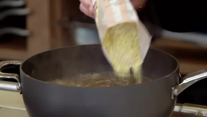 Aggiungere lentamente la polenta al liquido caldo, mescolando per evitare grumi (968.519).