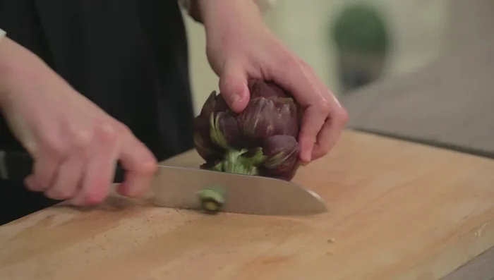 Pulire i carciofi: rimuovere la parte coriacea del gambo e le foglie esterne più dure, fino a raggiungere le foglie più tenere. Spuntare la cima del carciofo.