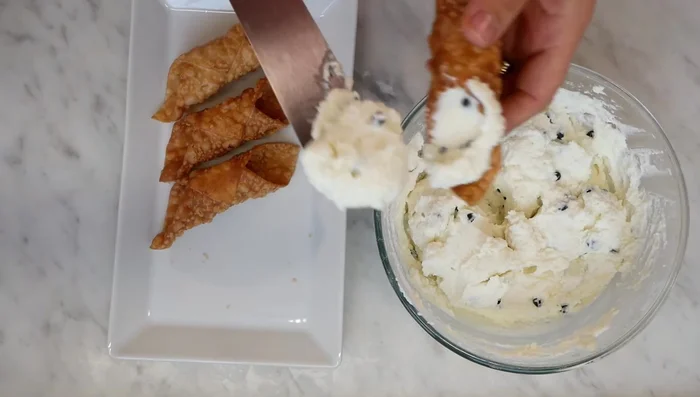 Riempire i cannoli: Riempire i cannoli con la crema di ricotta usando una spatola o una sac à poche. [330.87]
