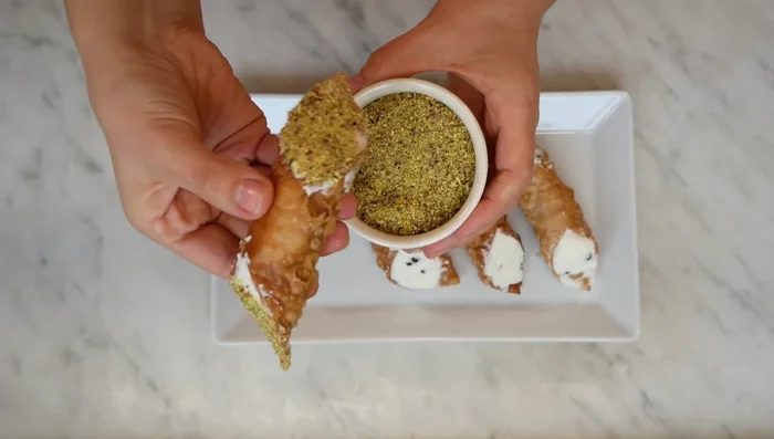 Guarnire e servire: Guarnire i cannoli con canditi di arancia, ciliegie candite, gocce di cioccolato o zucchero a velo. [354.62]