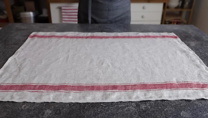 Stendere la pasta: Infarinare abbondantemente il canovaccio e stendere la pasta su di esso con il mattarello, formando un rettangolo di 50x35 cm.