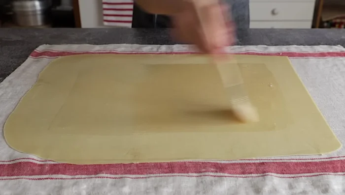 Assemblare lo strudel: Spalmare la pasta con burro fuso e pangrattato rimanente. Distribuire la farcitura di mele, lasciando liberi 5 cm dai bordi. Aggiungere pinoli e uvetta.