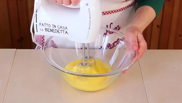 In una ciotola capiente, sbatti le uova con lo zucchero fino ad ottenere un composto spumoso. Aggiungi l'olio e continua a mescolare.