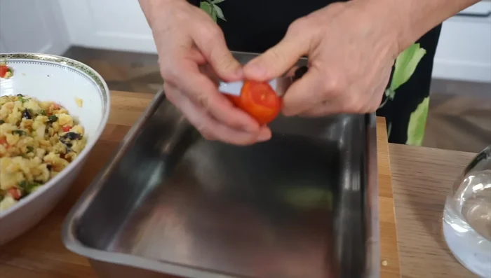 In una teglia, disporre delle rondelle di pomodoro, aglio tritato, prezzemolo, olio e sale. Aggiungere acqua (circa mezzo centimetro).