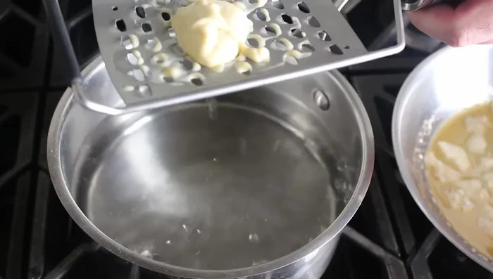 Cuocere gli spätzle: Portare a ebollizione abbondante acqua salata. Usando una grattugia (lato liscio), spingere la pastella nell'acqua bollente. Gli spätzle sono cotti quando galleggiano in superficie. (209.28)